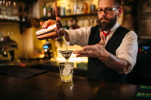 Barman flaring behind bar counter. Restaurant shelves with alcoholic drinks bottles on background