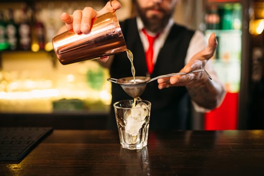 Barman flaring behind bar counter. Restaurant shelves with alcoholic drinks bottles on background