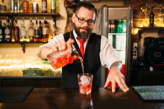 Barman pouring alcoholic drink in glass. Bartender flairing in restaurant