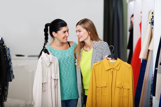Happy women talks holding cute dresses in the shop