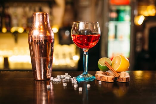 Beverage in glass, shaker, lime, lemon, salt and dice on wooden bar counter