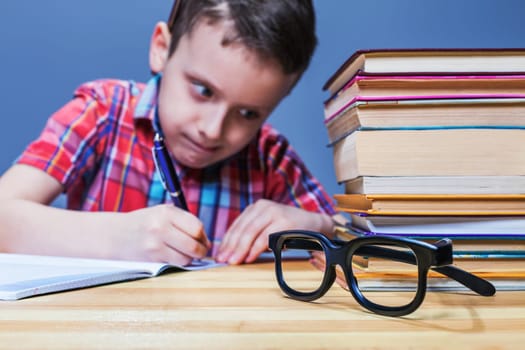 Pensive schoolboy study at school, homework learning. Pupil in glasses against books
