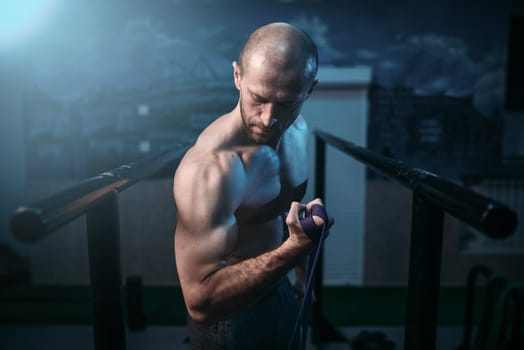 Muscular sports man exercises with elastic rubber band. Active sport lifestyle. Male strong biceps