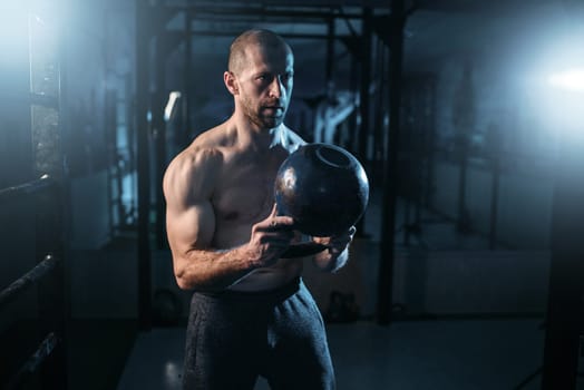 Strong weightlifter workout with kettlebell in gym. Man with muscular torso training with weight
