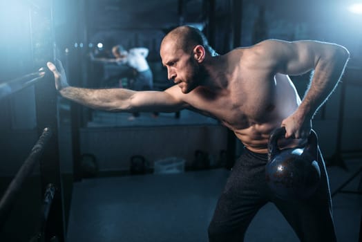 Muscular athlete workout, man lifting kettlebell. Strong sportsman training with weight
