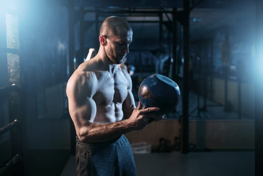 Strong weightlifter workout with kettlebell in gym. Man with muscular torso training with weight