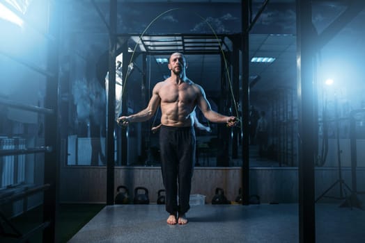 Muscular athlete exercises with jump rope in gym. Sportsman on fitness training. Active sport lifestyle