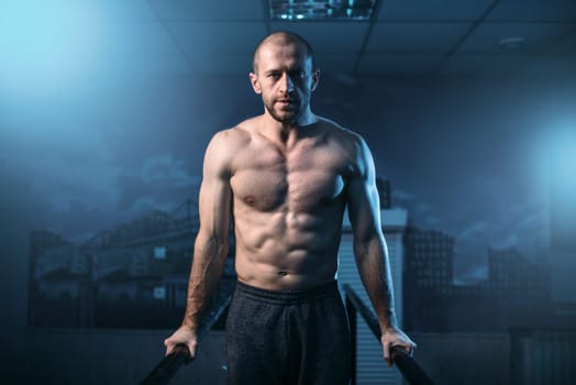 Muscle gymnast exercises on sports bars in gym. Strong athlete on gymnastic training