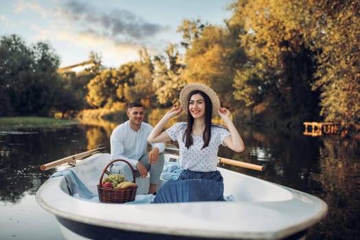 Love couple with fruit basket in boat on quiet lake at summer day. Romantic date, boating trip, man and woman walking along the river
