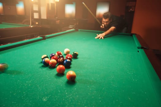 Player breaks a pyramid in billiards. Nightlife. Billiard room on the background.