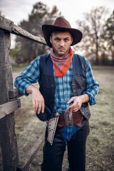 Brutal cowboy with cigar in the horse corral, texas ranch, western. Vintage male person with gun on farm, wild west lifestyle