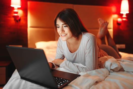 Woman lying in bed and looking on laptop screen, good morning, bedroom interoir on background. Lady awake