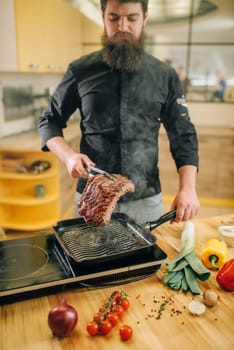 Male person cooking meat in a pan on the kitchen. Man preparing boiled pork
