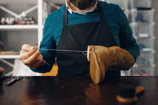 Shoemaker stitches the shoe, footwear repair service. Craftsman skill, shoemaking workshop, master works with boots, cobbler job