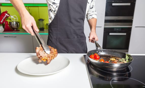 Young man putting fried meat to the plate at home kitchen