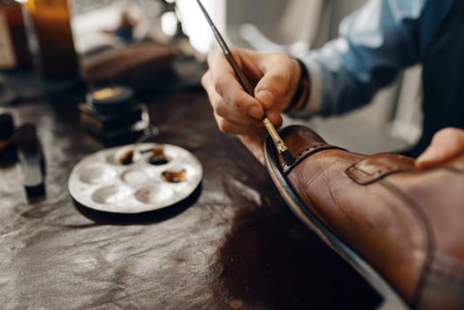 Shoemaker with brush tints shoes, footwear repair service. Craftsman skill, shoemaking workshop, master works with boots, cobbler