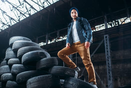 Stalker, traveler climbs a mountain of tires, abandoned factory. Danger zone