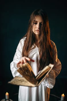 Young woman in white shirt sitting in the center of pentagram circle with candles and reads a spell, black wooden floor, smoke all around. Dark magic ritual, occultism