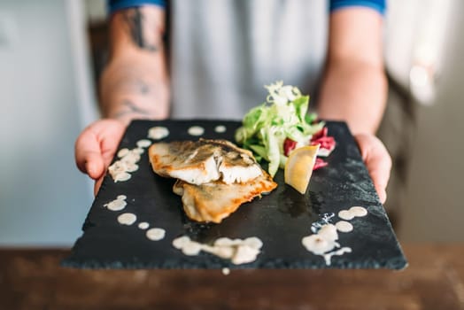 Male hands hold dish of fried fish fillet decorated with vegetables. Fresh grilled seafood. Gourmet delicious dinner concept