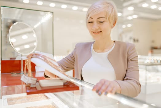 Woman choosing golden necklace at the showcase in jewelry store. Female person buying gold decoration in jewellery shop