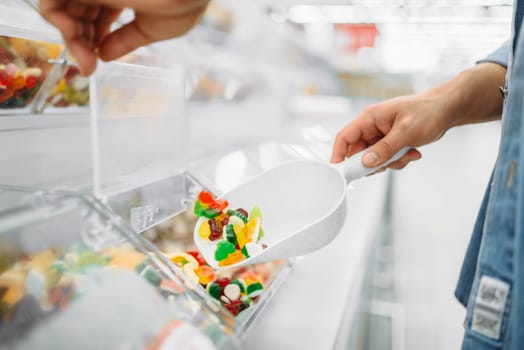 Male person picks up a package of chewy candy in a supermarket, family shopping. Customer buys marmalade in shop, buyer in market, sweets department
