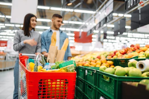 Couple with cart in supermarket, fruits department, family shopping. Customers in shop, buyers in market