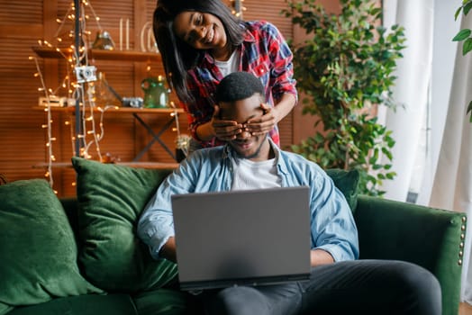 Black couple with laptop having fun on sofa at home. Happy african love couple leisures in their house, cheerful family relaxing in living room