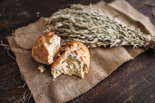 Fresh baked bread loaf with crispy crust breaked in half and wheat bunch on burlap cloth. Homemade bakery concept, natural organic food.