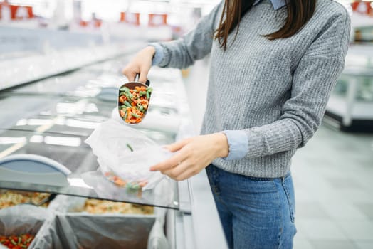 Woman picks up a package of frozen vegetables in a supermarket, family shopping. Female customer buys products in shop, buyer in market