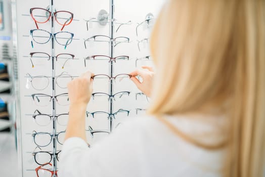 Female optometrist shows glasses in optics store. Selection of eyeglasses with professional optician