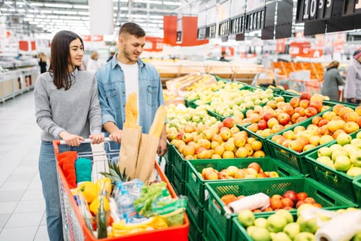 Couple with cart in supermarket, fruits department, family shopping. Customers in shop, buyers in market
