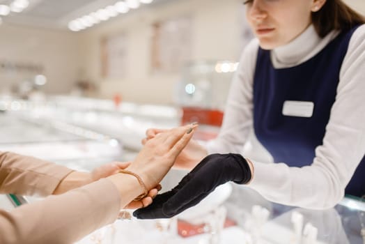 Woman trying on gold bracelet at the showcase in jewelry store. Female person buying golden decoration in jewellery shop