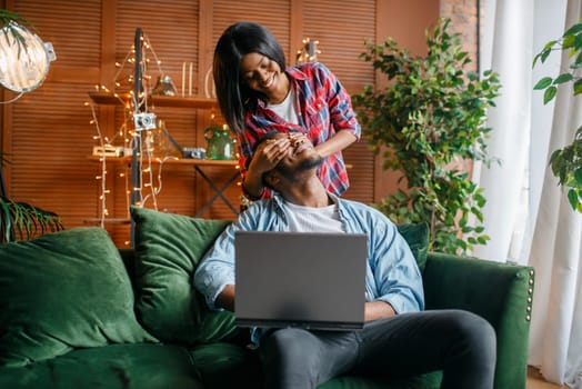 Black couple with laptop having fun on sofa at home. Happy african love couple leisures in their house, cheerful family relaxing at home