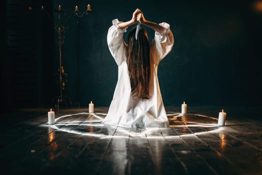 Woman with knife in hands sitting in pentagram circle with candles. Dark magic ritual, occultism and exorcism, supernatural power
