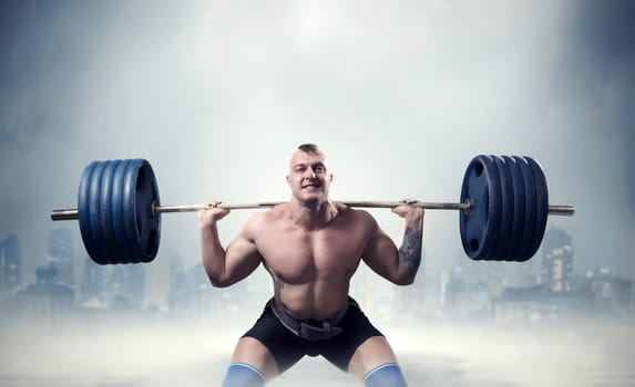 Muscular male weightlifter exercise with barbell, dark cityscape on background