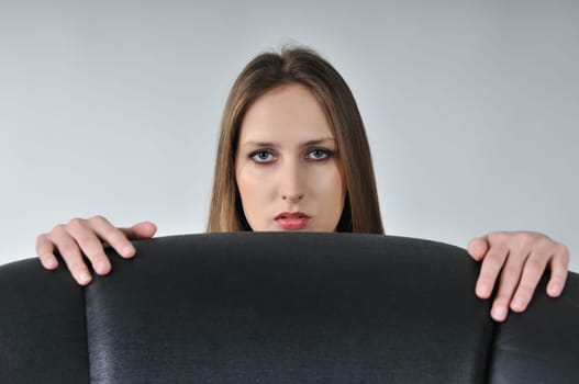 Studio portrait of young woman hidden behind big black armchair - face with hands visible