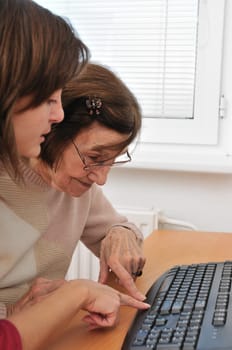 Young woman teaches her grandmother work with computer - senior lifestyle