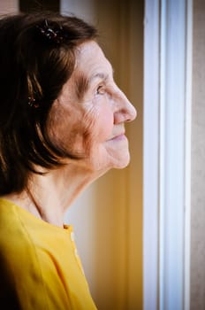 Solitude concept  - sad 80s senior woman looking through window at home
