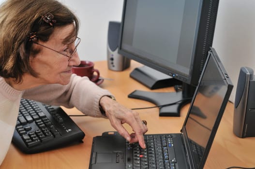 80-something senior woman working with laptop, another computer in the background