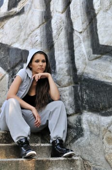 Young person (teenagerl) in hip hop style siting on stairs in front of black and white graffity wall
