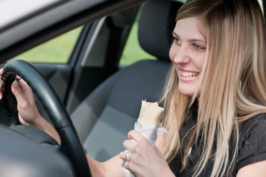 Young beautiful smiling woman driving car and eating fast food - portrait through side window