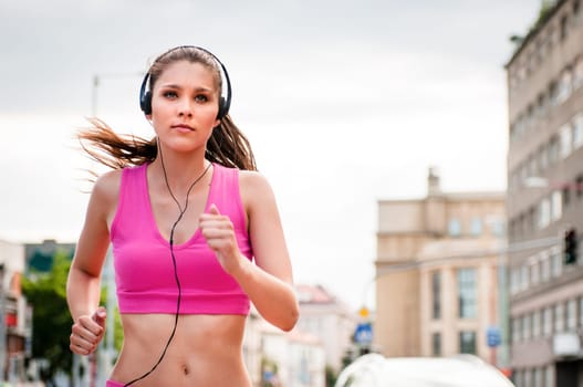 Young beautiful woman with headphones jogging and listening music in street