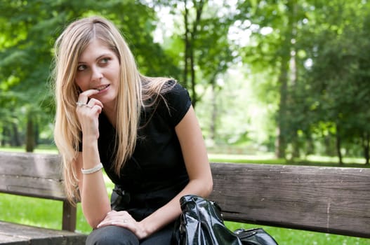 Portrait of young beautiful flirting woman siting on bench in park outside