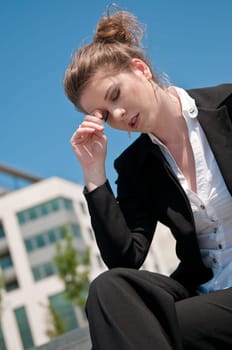 Young depressed business woman siting outdoors - building in background