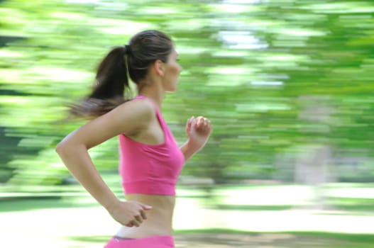 Young person (woman) running outside in park on sunny day - motion blurr