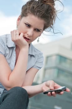 Young worried woman with unhappy expression holding mobile phone - outdoors in urban setting