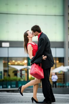 Young business couple dressed in red kiss and welcome each other on street