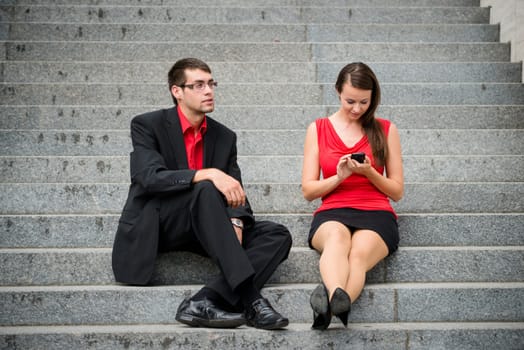 Young business woman sitting on stairs and working with smartphone while man is bored and angry
