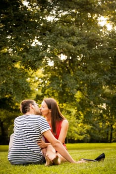 Young smiling couple sitting and kissing on grass - woman barefoot with shoes next to her