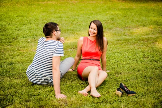 Young smiling couple sitting and talking on grass in park on date